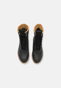 Botas altas de cuero negro con forro de ante marrón, punta redonda y cordones planos. Suela de goma con un agarre texturizado y costuras en contraste.