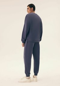 Granatowy dres wykonany z miękkiego materiału, z okrągłym dekoltem, ściągaczami przy rękawach oraz zwężanymi spodniami w połączeniu z białymi trampkami.