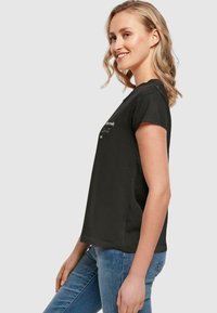 Svart t-skjorte med korte ermer og rund hals, med hvit tekst trykket på fronten. Brukt med lyseblå jeans.