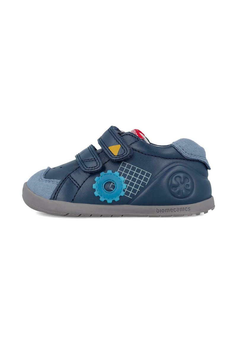 Zapato infantil azul marino con acentos grises, dos correas de velcro, patrones de engranaje y cuadrícula, y una suela flexible gris. Fabricado con material sintético texturizado.