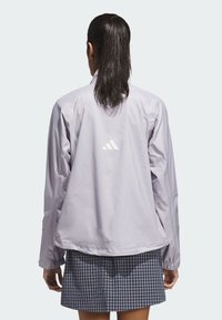 Light purple waterproof jacket with elastic cuffs, featuring a reflective logo on the back. Paired with a plaid skirt.