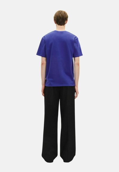 Lila Baumwoll-T-Shirt mit kurzen Ärmeln und Rundhalsausschnitt, kombiniert mit weiten schwarzen Hosen. Einfaches Design, keine sichtbaren Muster oder Logos.