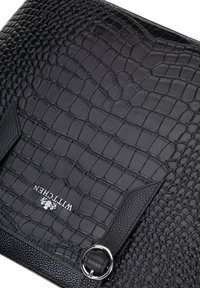 Zwarte leren handtas met een gestructureerd krokodillenpatroon, soepele accenten, zilveren hardware en een cirkelvormige ringdetails. Merkenlogo geperst.