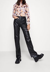 Schwarze Kunstlederhosen mit hoher Taille und weitem Bein, kombiniert mit einem gemusterten Langarmoberteil mit floralen Design in Orange und Lila.