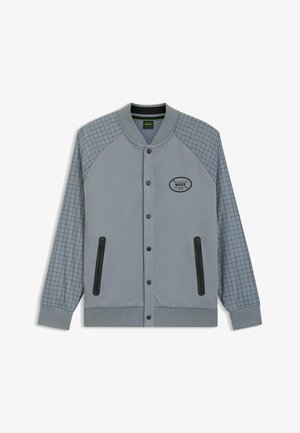 Grå sportsjakke med en struktureret krop og ærmer med ternet mønster. Har trykknapper og to sidelommer med lynlås.