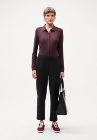 Haut bordeaux à manches longues et à boutons ; pantalon noir à rayures avec une poche ; baskets bordeaux et crème ; sac fourre-tout noir.