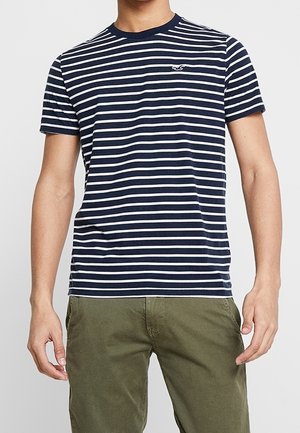 T-shirt bleu marine à manches courtes avec des rayures blanches horizontales, col rond et un petit logo sur le haut de la poitrine à gauche.