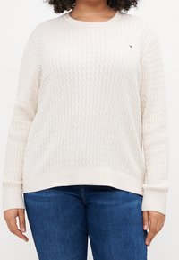 Maglione crema con lavorazione a punto diamante, scollatura a girocollo e polsini a coste. Abbinato a jeans blu scuro.