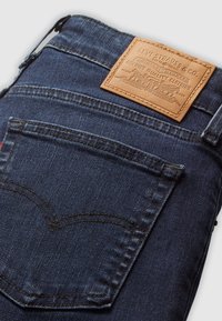 Jean en denim bleu foncé montrant la poche arrière et la pièce en cuir fauve de la marque Levi Strauss & Co. avec logo et texte.
