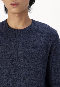 Suéter de punto azul marino con un acabado texturizado y cuello acanalado. Presenta un logo sutil en el pecho.
