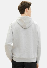 Sudadera con capucha gris, fabricada en una tela suave, que presenta una costura central en la parte posterior, puños y bajo acanalados, con un ajuste relajado y una capucha espaciosa.