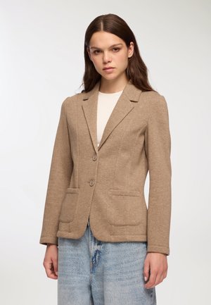 Blazer beige in tessuto testurizzato, vestibilità su misura, chiusura con un bottone, colletto a rever e due tasche frontali. Abbinato a denim chiaro.
