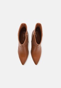 Brune lær ankle boots med spidse tæer, buet design og sidelukninger. Glat tekstur og minimal syning.