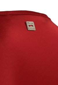 Top in tessuto rosso con texture liscia. Presenta un'etichetta quadrata argentata con la scritta "Manila Grace" sul collo sul retro. Design semplice.