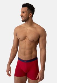 Boxer da uomo rossi realizzati in tessuto morbido con un elastico navy in vita che presenta un logo. Progettati per offrire comfort e una vestibilità aderente.