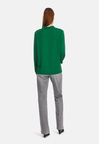 Green long-sleeve blouse with a collar, featuring a smooth texture; paired with light gray straight-leg jeans and black heels.
