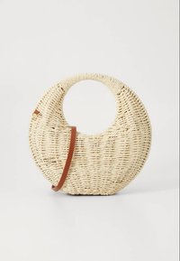 Kerek szövött szalmakézitáska kör alakú fogóval, kontrasztos barna vállpánttal, természetes textúrát és világos színt bemutatva.