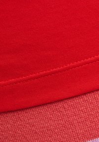 Rode stof met een gladde, iets geribde textuur, met een contrasterend element in een lichtere schaduw van rood eronder.