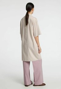 Stribet oversized skjorte i beige med lilla striber, med korte ærmer; parret med lyserøde vide bukser. Casual stof.