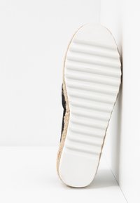 Chaussure espadrille noire avec une semelle texturée enveloppée de jute et un fond en caoutchouc blanc. La forme est plate, avec un bout arrondi et un design profilé bas.