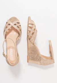 Sandali con tacco a forma di cuneo d'oro con cinturini incrociati, texture in suede e metalliche, punta aperta, cinturino alla caviglia regolabile e suola solida color tan.
