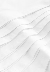 Tissu blanc avec des plis doux et ondulés, doté d'une texture lisse et de détails de couture fins, créant une apparence en couches.