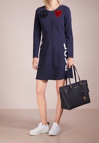 Laivastonsininen mekko pitkillä hihoilla, jossa on rauha- ja sydämen aplikaatiot, valkoinen "LOVE"-teksti ja kapea siluetti. Yhdistetty mustan olkalaukun kanssa.