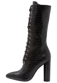 Botte noire mi-mollet avec motif crocodile, bout pointu et talon aiguille. Présente un laçage avec des œillets dorés.