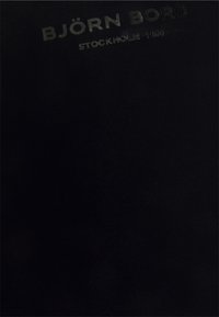 Črn material z logotipom "BJÖRN BORG" in "STOCKHOLM 1984" embosirani v subtilni, kontrastni barvi. Gladka, elastična tekstura.
