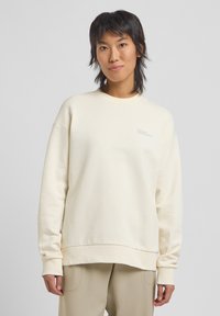 Felpa color crema con girocollo e maniche lunghe. Presenta una vestibilità comoda e un piccolo logo sul petto. Texture liscia.