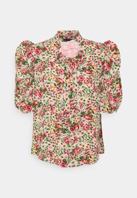 Blouse florale avec des manches bouffantes, ornée d'une accent de fleur rose sur le col. Le tissu a un fond clair avec des motifs rouges, roses et verts.