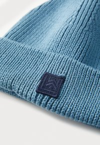 Gebreide muts in lichtblauw, met een ribbelstructuur en een marineblauw vierkant patch met een reliëfontwerp aan de zijkant.