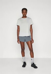 Lys grå kortermet treningsskjorte med rund hals, kombinert med mørkegrå shorts og svarte joggesko. Ingen synlige mønstre eller detaljer.