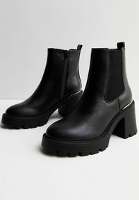 Stivaletti ankle in pelle nera con tacco spesso, pannelli laterali elasticizzati e zip frontale. Presentano una suola testurizzata e minime rifiniture metalliche.