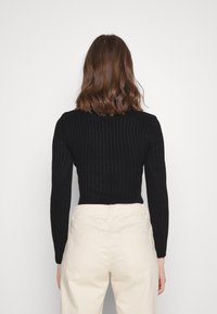 Czarny prążkowany top z długim rękawem z dopasowaną talią, zestawiony z jasnymi, wysokim stanem spodniami. Gładka tekstura i dopasowany krój.