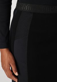 Zwarte sportrok met een gestructureerd netpaneel, gladde stof en een elastische tailleband met merk. Close-up weergave van de zijkant en de hand.