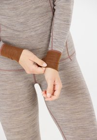 Brun och grå långärmad topp med kontrasterande bruna manschetter, med en strukturerad tyg och synliga sömnadsdetaljer.