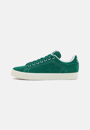 Zapatilla de ante verde con suela de goma blanca, punta redonda y seis ojales. Acentuada con detalles perforados y marca en el talón.