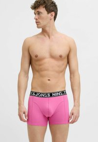 Roze bokserice od mekanog materijala s crnim pojasom na kojem se nalazi bijeli natpis. Dizajn uključuje prilagođen oblik i šivene detalje.