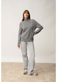 Szary sweter z golfem o splocie w warkocze, z prążkowanymi mankietami i dół, w zestawie z jasnoszarymi spodniami typu wide-leg oraz wzorzystymi trampkami.