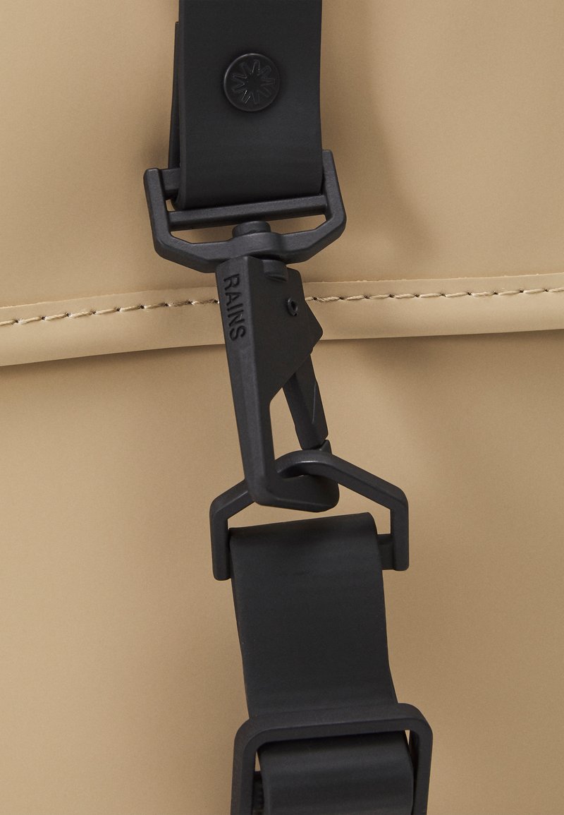 Boucle et sangle en plastique noir sur un fond beige, avec une texture lisse et un design minimal, mettant en avant des détails de quincaillerie épurés.