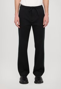 Black sweatpants with a drawstring waistband, featuring green side stripes, a relaxed fit, and smooth fabric texture.