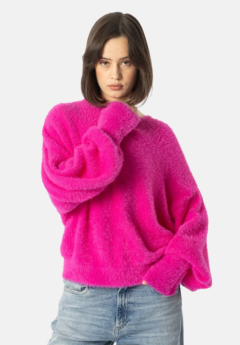 Maglione rosa fluffy con una vestibilità ampia e maniche larghe, caratterizzato da un colletto a girocollo e una texture morbida. Abbinato a jeans azzurri.