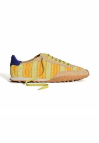 Zapatilla de cordones con parte superior de punto en amarillo y verde, detalles de ante y suela de goma marrón claro con agarre texturizado.