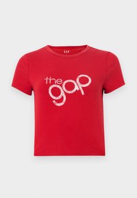 Rode katoenen T-shirt met korte mouwen, ronde hals en een groot glinsterend wit tekstlogo "the gap" in het midden. Eenvoudig ontwerp, geen patronen.