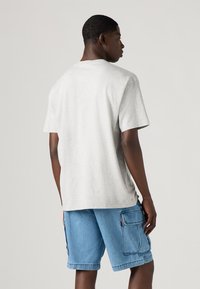 T-shirt de algodão cinza com um corte relaxado, mangas curtas e bainha reta, combinado com calções de ganga azul claro com bolsos de carga.