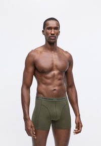 Olívazöld bokszernadrág, puha anyagból, sötét derékrésszel, amelyen a "BJÖRN BORG" márkaneve látható, és testhezálló fazonnal.