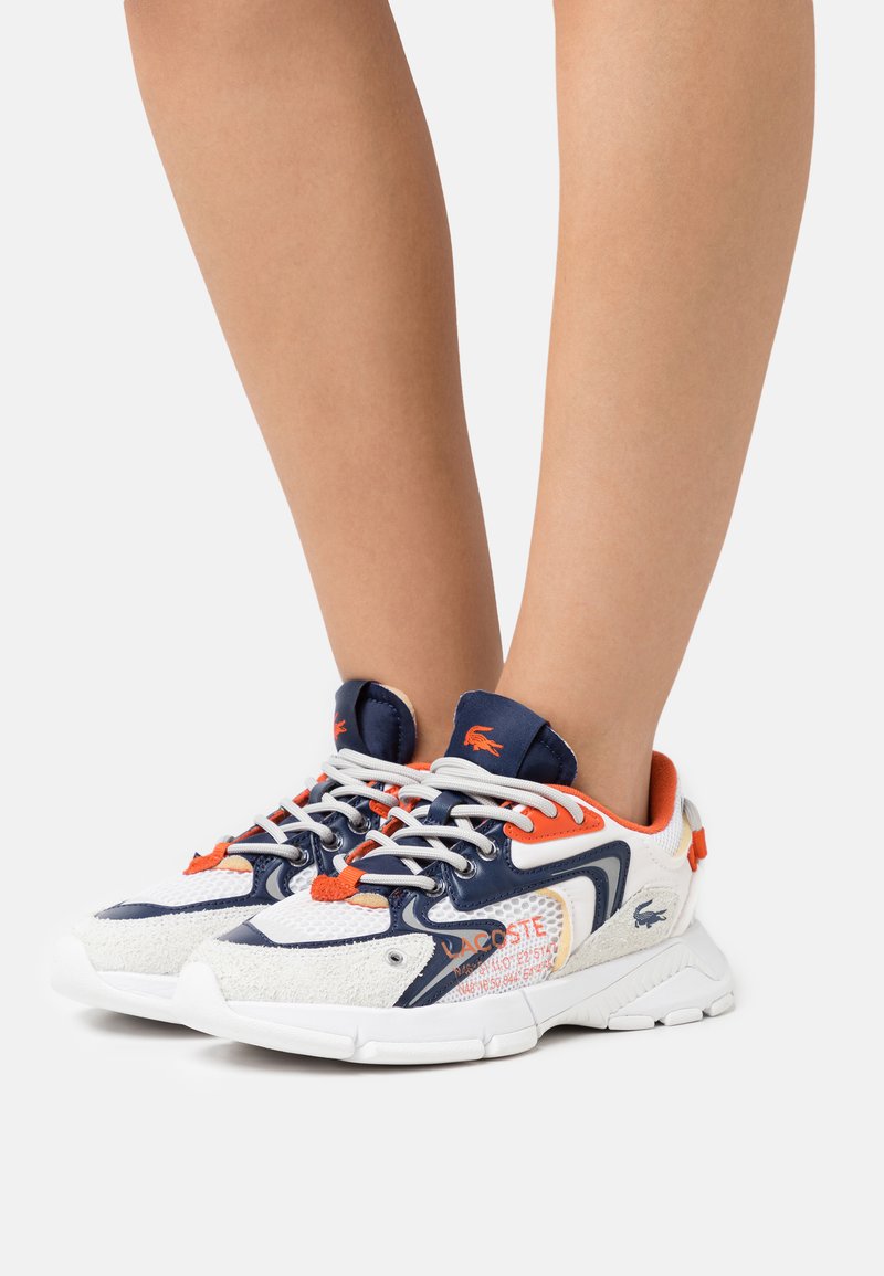 Tenisky Lacoste s bílou a námořnickou síťovinou, oranžovými akcenty, texturovanými detaily a logem. Mají silnou bílou podrážku a šněrovací uzávěr.