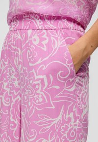 Tissu rose à motifs avec de légères fleurs, doté d'une taille élastique et de détails de poches latérales. Matériau doux au toucher.