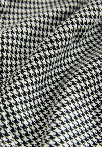 Tessuto a motivo pied-de-poule nero e bianco con una superficie strutturata, caratterizzato da un disegno tessuto che crea profondità e dimensione.